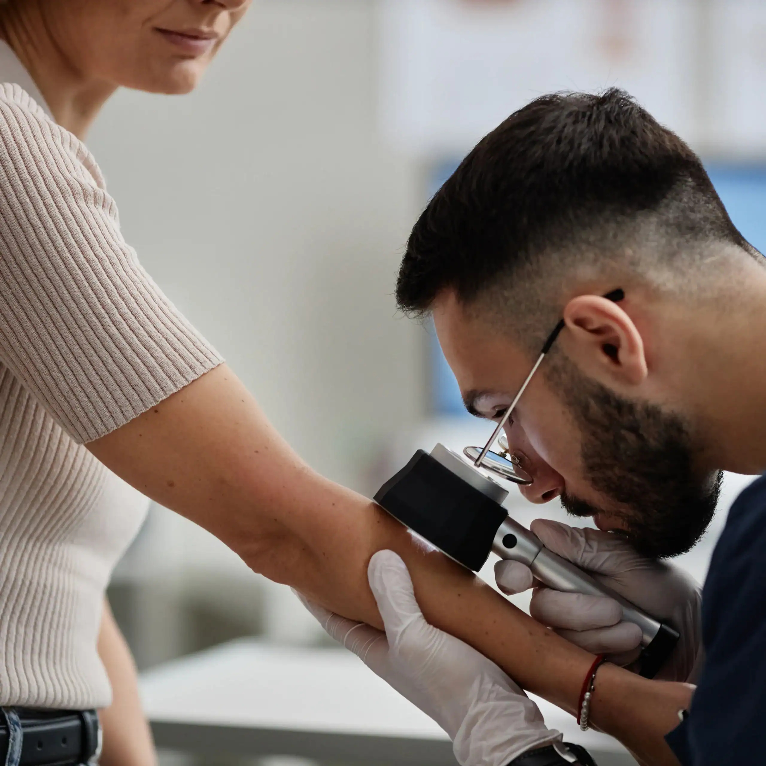 A dermatologist uses a dermatoscope or surface microscope to examine a spot on a woman's arm