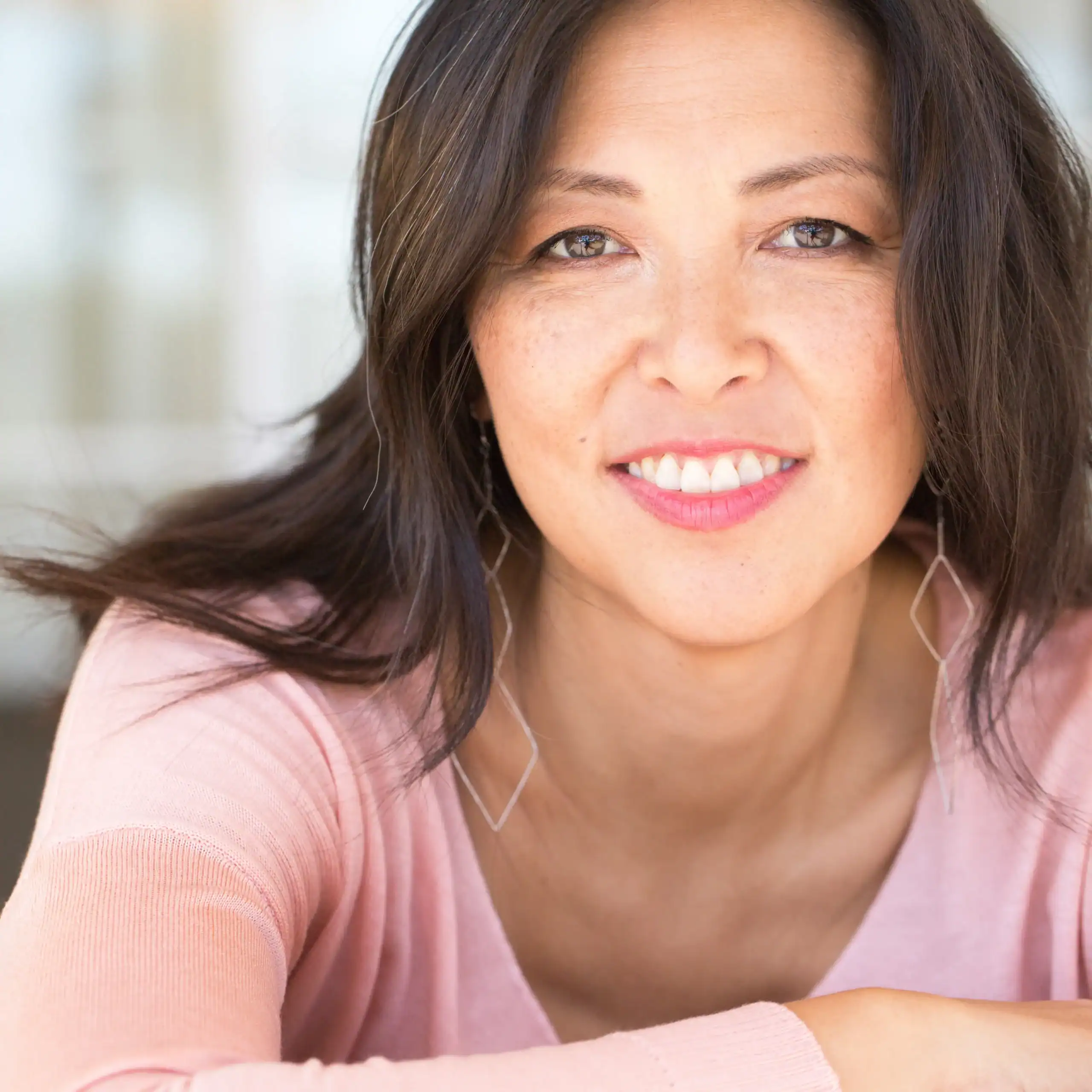 Woman with light freckles and a pink shirt smiles for the camera