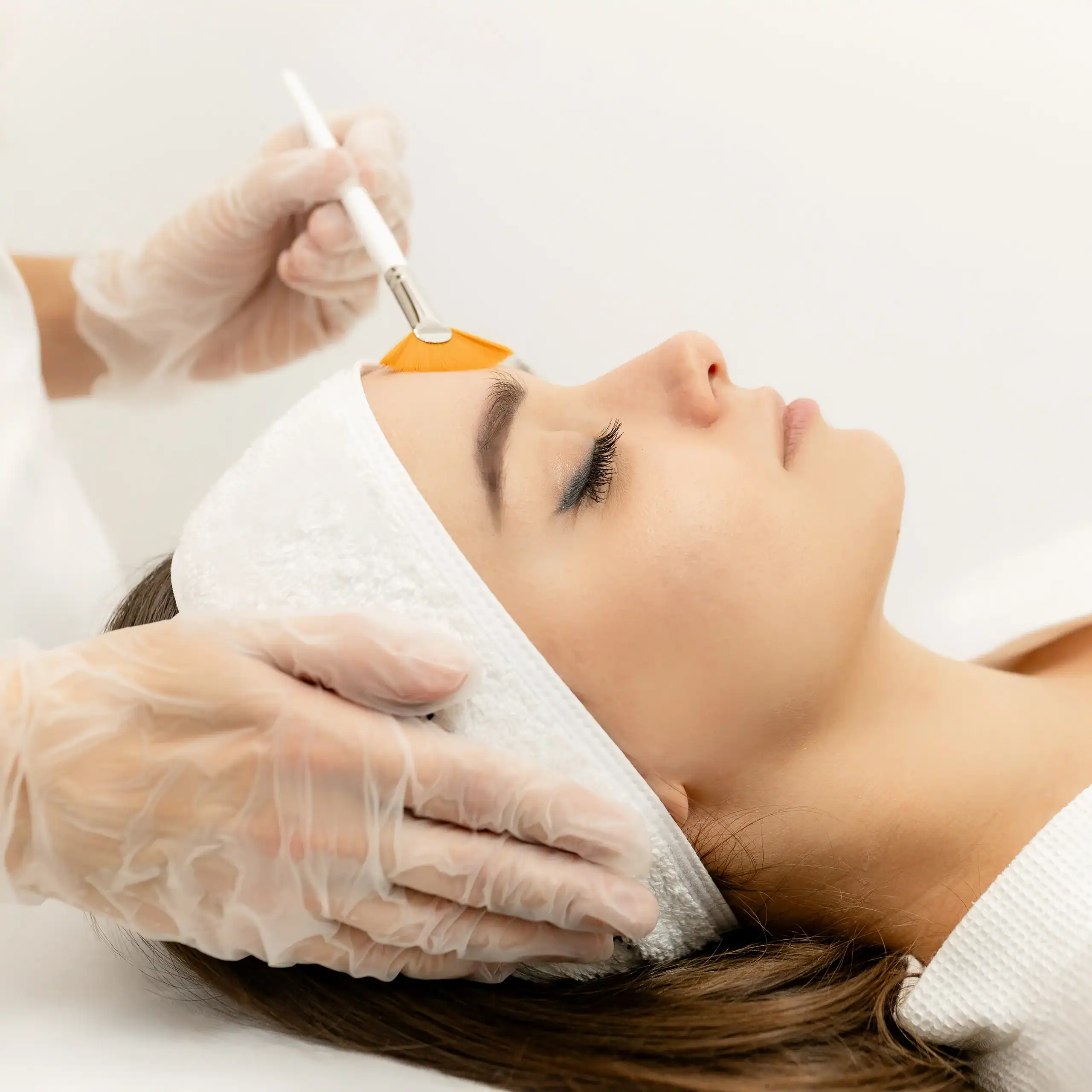 An aesthetician applies a chemical peel treatment to you a young woman.