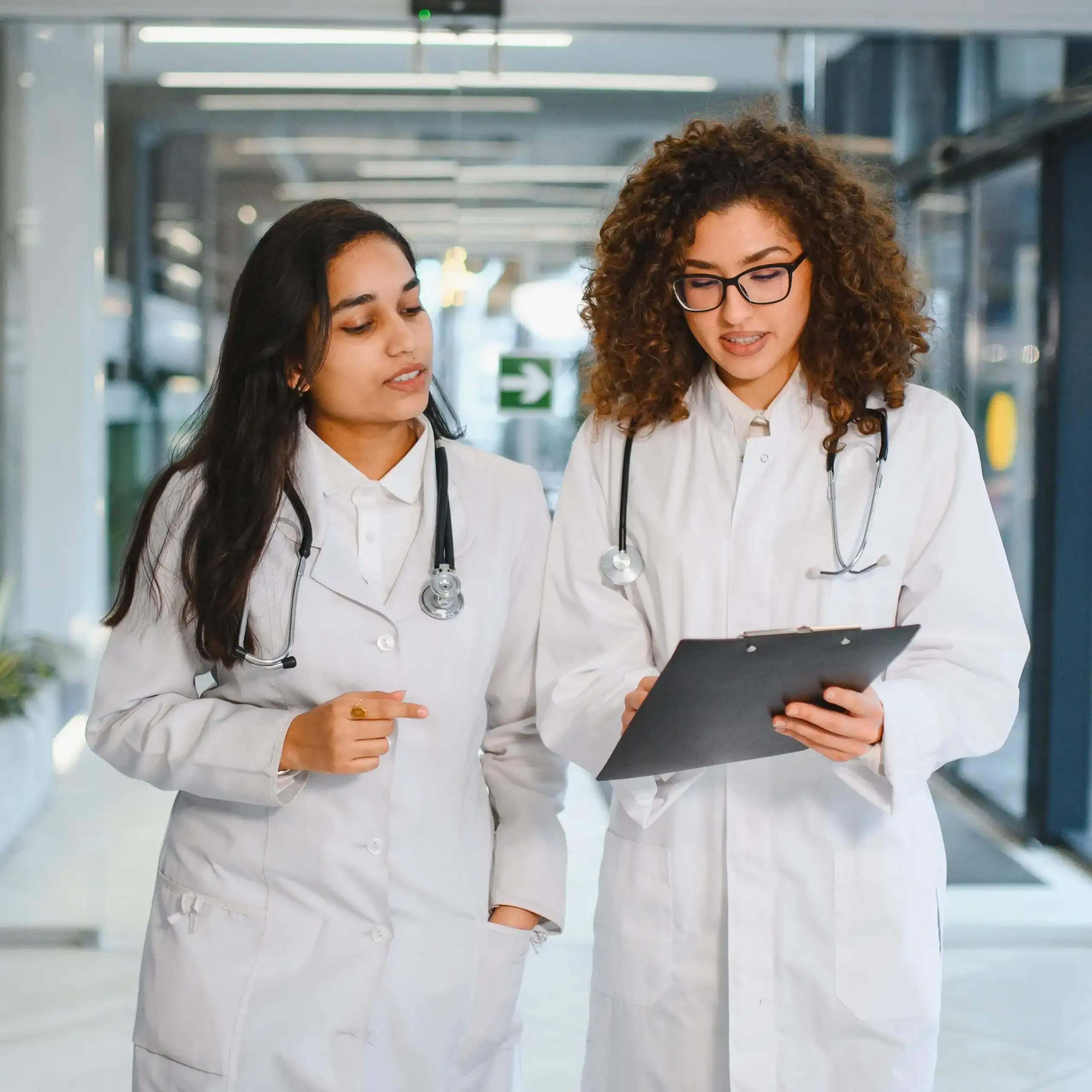 Dos médicos jóvenes caminan por el pasillo hablando de un caso