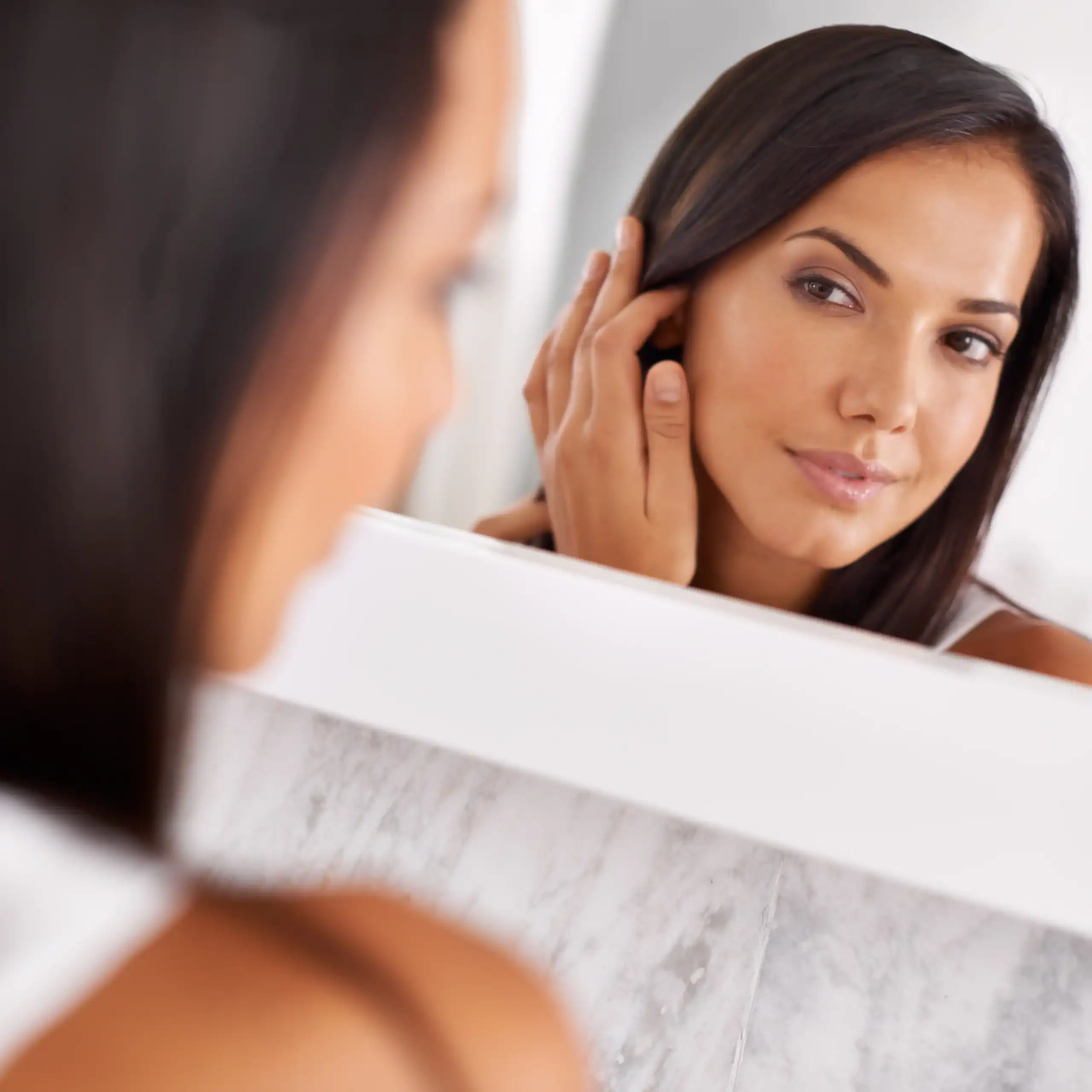 Woman with beautiful skin looks at her reflection in the mirror