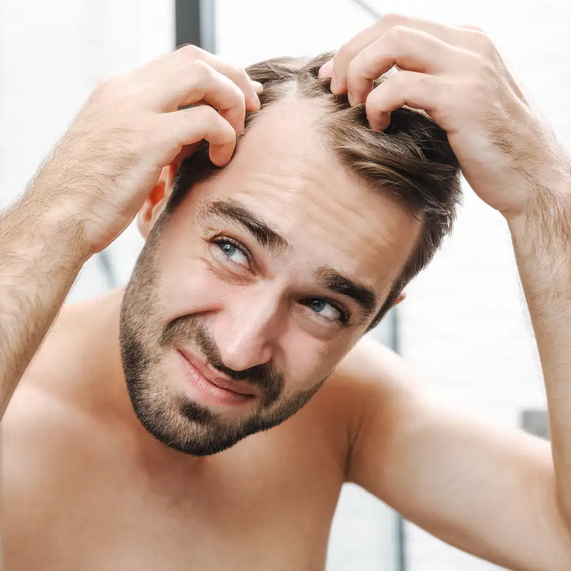 Young man looks in the mirror and inspects an area where he has hair loss.