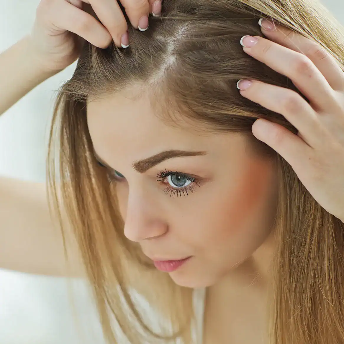 Young woman inspects her hair for hair loss in the mirror.