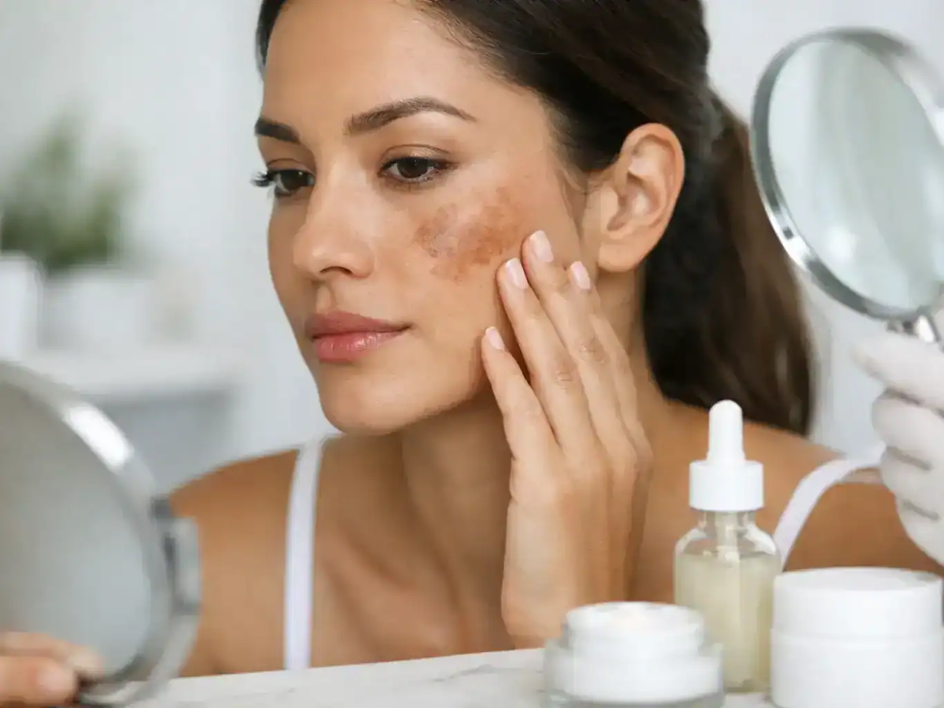 woman looks at melasma spot on her face in a mirror